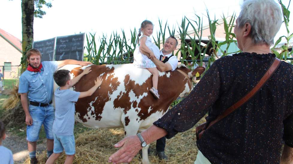 Melkveehouder Silvain Kusters (achter de koe) en zijn medewerker Jaap (links) tonen niet alleen de hoeveelheid voer en water dat een koe dagelijks verorbert, maar bieden kinderen ook een speciale zit.