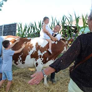 Melkveehouder Silvain Kusters (achter de koe) en zijn medewerker Jaap (links) tonen niet alleen de hoeveelheid voer en water dat een koe dagelijks verorbert, maar bieden kinderen ook een speciale zit.