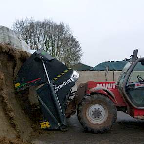 De veehouder vertelt dat hij net een nieuwe kuilhapper van Trioliet heeft gekocht. „Eerder laadde ik de mengwagen met een ‘pelikaanbak’ zonder messen.” Hij demonstreert de nieuwe kuilhapper bij de graskuil. Deze hapt in één keer een hele laag van boven na